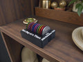 May include: A black coin holder with the text "One Day at a Time" and "Julie 20th November 2025" in white. It holds a variety of colourful coins and a silver coin. The holder sits on a wooden shelf, with other decorative items in the background.