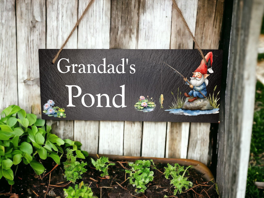 May include: Black slate sign with white text that reads "Grandad's Pond". A cartoon gnome with a red hat is fishing in a pond with lily pads and a fish.
