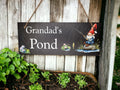 May include: Black slate sign with white text that reads "Grandad's Pond". A cartoon gnome with a red hat is fishing in a pond with lily pads and a fish.