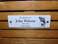 May include: White memorial plaque with black text that reads "In memory of John Webster 1965 - 2023 Gone Fishing". A colourful image of a trout jumping out of the water is on the right side of the plaque.